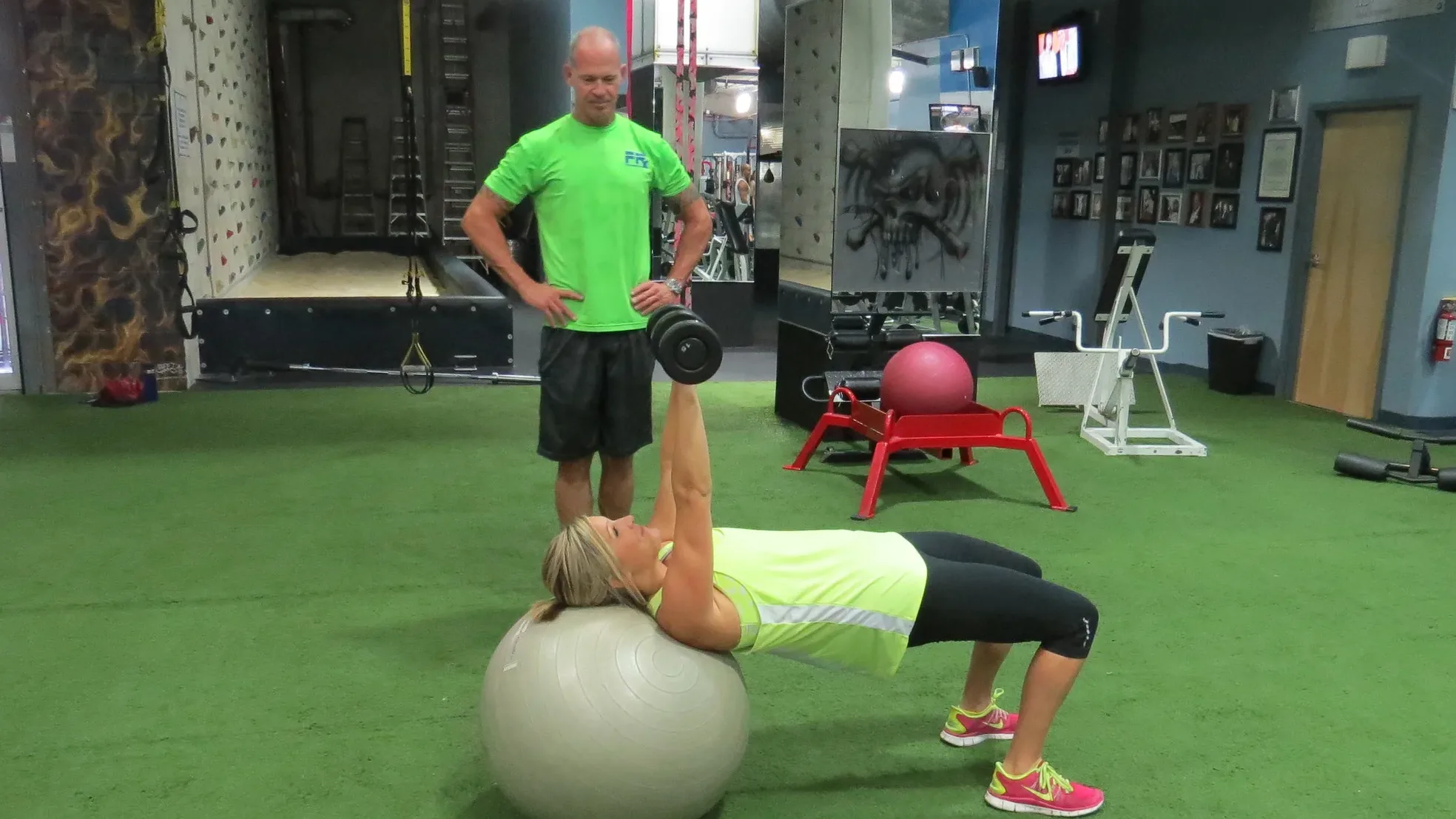 Tampa personal trainer Craig Chapin standing over a client as she holds a hip bridge on a stability ball and presses a dumbbell, watching the rep