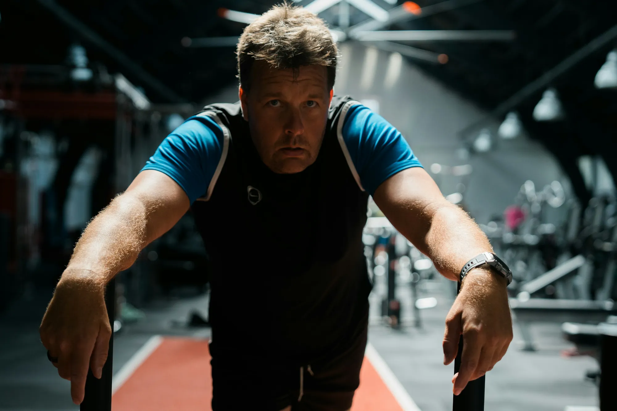 A man in his fifties leaning into a weighted sled on a turf lane mid-push: strength and conditioning for men over 50 with no jumping