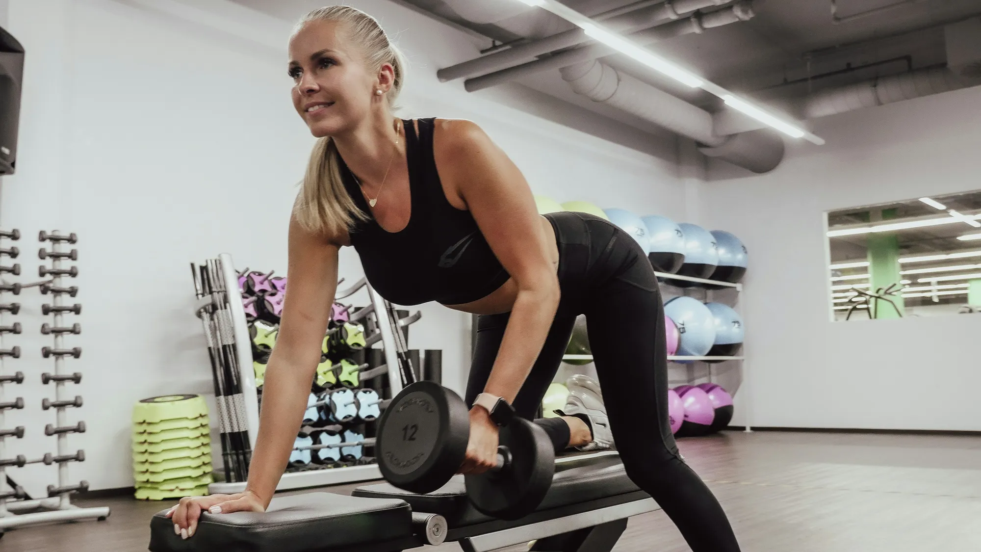 A woman braced on a weight bench rowing a heavy dumbbell in a bright gym, the kind of strength training that weight loss after 40 is built on