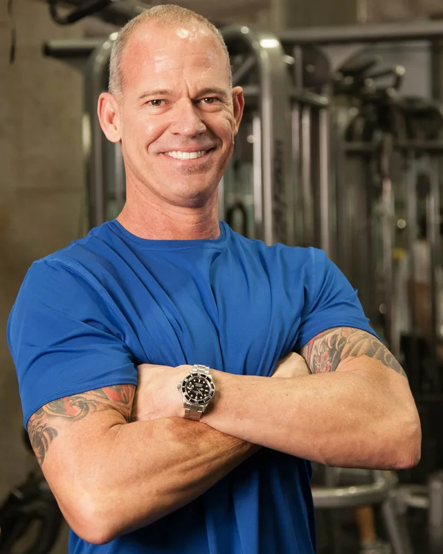 Craig Chapin standing with his arms folded, smiling, in front of the cable machines at Empire MMA and Fitness