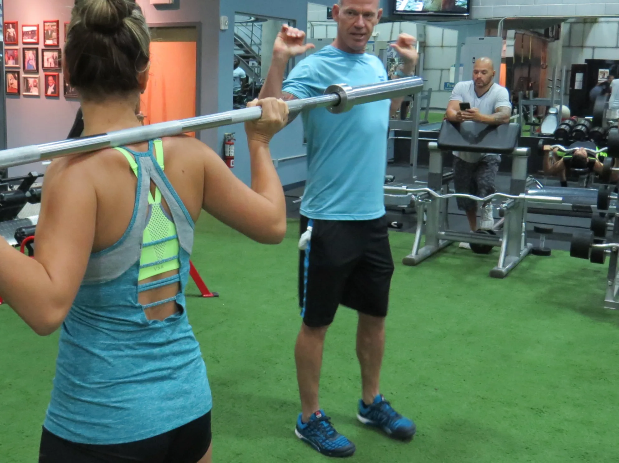 A personal trainer coaching a woman through a front-racked barbell lift on the gym floor in South Tampa, talking her through the set