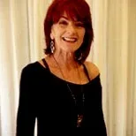 Sherry smiling in a black off-shoulder top, photographed against a white curtain